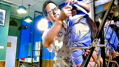 Chinese BDSM teaser: bound woman in blue dress with dominant man adjusting ropes