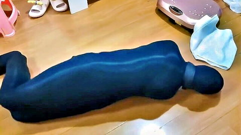 Bound woman encased in shiny black latex catsuit lying prone on floor in BDSM bondage