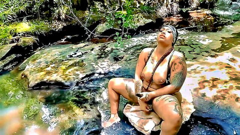 Tattooed ebony MILF squats nude spreading legs exposing pussy in forest stream