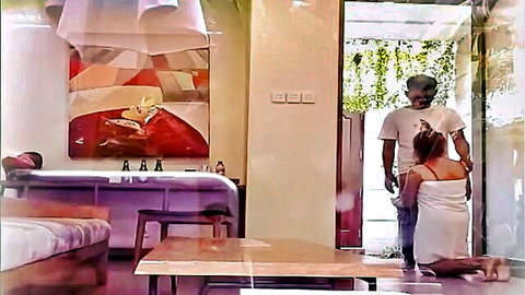 Indonesian man stands behind kneeling woman in short white dress in hotel room threesome tease