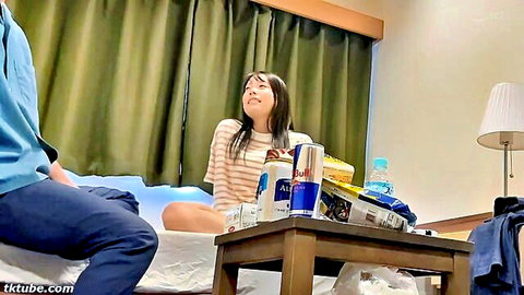 Asian couple in hotel room, woman in striped top sitting on bed looking up at man