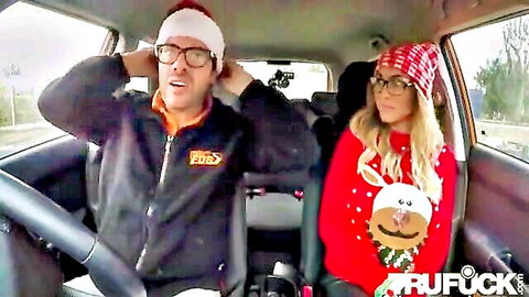Grinning Santa hat guy and blonde in reindeer sweater smile excitedly in car on road