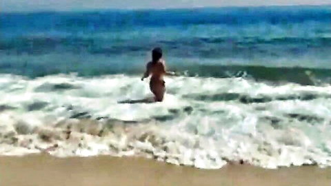 Brazilian MILF in black bikini walking into ocean waves on beach vacation