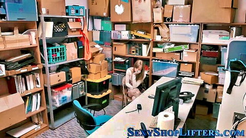 Young clothed shoplifter sits in cluttered stockroom office with boxes and computer