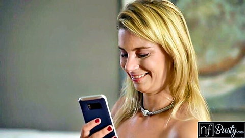 Busty blonde smiling at phone in teasing pose from cheating threesome video