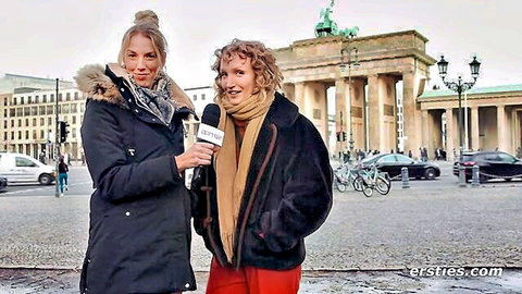 Blonde and curly-haired women in coats holding erot ies mic at Brandenburg Gate