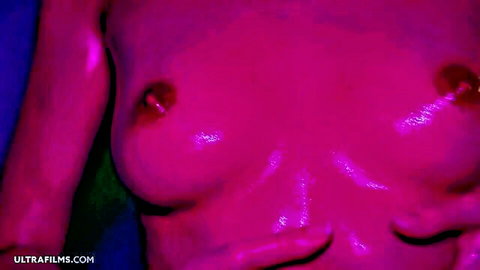 Closeup of shiny oiled tits with erect pink nipples glowing in sensual purple light