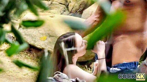 Brunette woman giving outdoor blowjob to muscular man in cuckold scene from Biggy Creek Bang