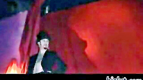 Man in black suit and hat performing energetically on dramatic red-lit stage with flames