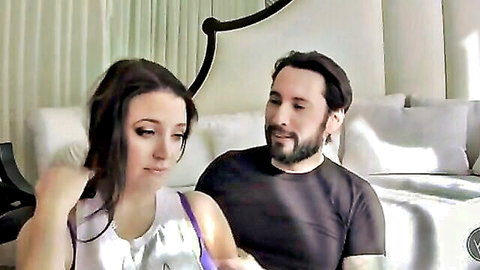 Brunette MILF in sheer white top sitting intimately with bearded stud on couch