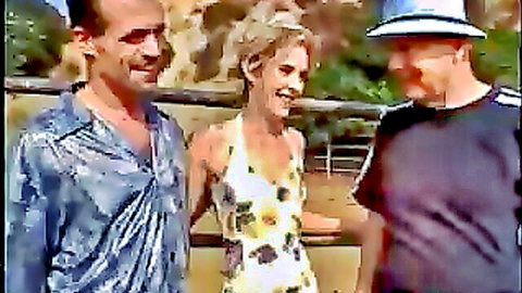 Smiling blonde MILF in yellow sundress posing happily with two grinning men outdoors