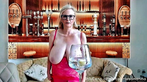 Big boobed blonde in low-cut pink dress holding wine glass, teasing cleavage