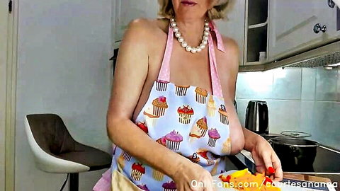 Mature blonde with huge natural tits exposes sideboob in cupcake apron chopping peppers topless