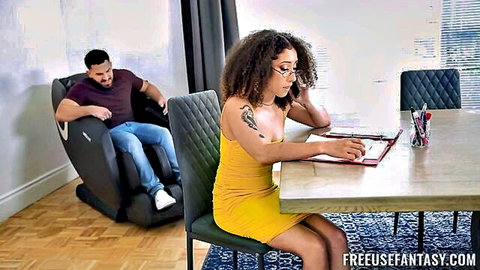 Curly-haired ebony stepdaughter in yellow dress studies at table while stepdad watches from behind