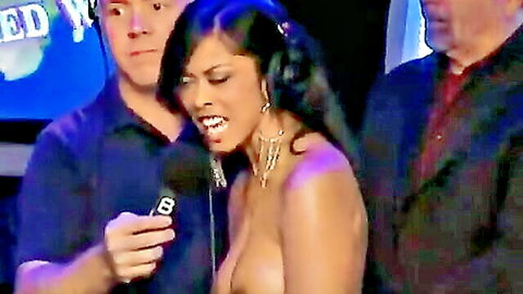 Topless ebony babe with huge bare tits holds mic onstage surrounded by men