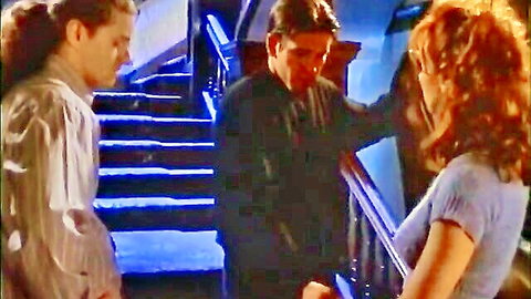 Redhead woman in low-cut top chats intimately with two men on neon-lit stairs
