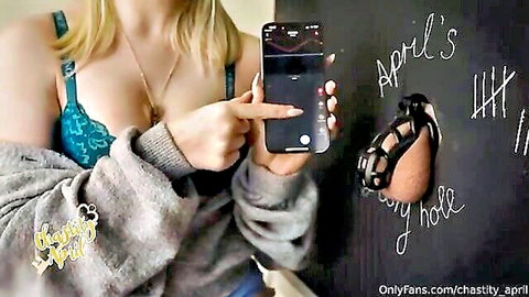 Busty blonde mistress April in cleavage-revealing bra points at glory hole chastity cage with exposed ass