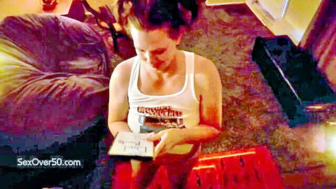 Mature brunette woman in tight tank top, sitting and reading book with surprised look