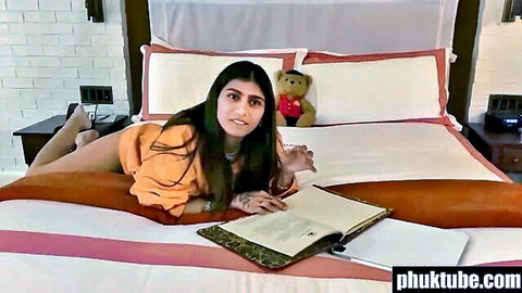 Curvy olive-skinned brunette with big tits teases on bed in orange romper holding teddy bear