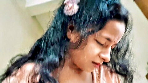 Sexy Indian babe with pink flower in long wavy black hair gazing sideways seductively