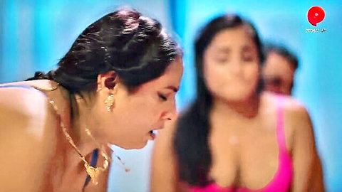 Busty Indian MILF in blue top puckers lips close to another big-titted woman in pink top