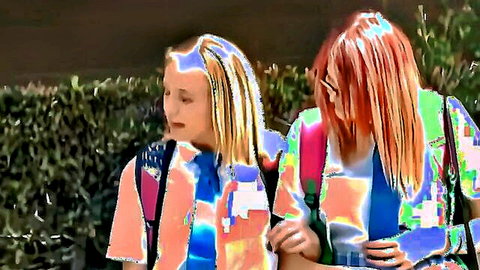 Skinny blonde and redhead teens in colorful tops and backpacks standing close outdoors