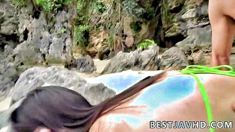 Busty Asian babe with big tits gets pussy fucked missionary on rocky beach in green bikini