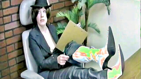 Femdom boss in black leather pants and colorful high heels holds clipboard smirking seductively