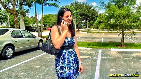 Sexy brunette in tight blue dress talking on phone in sunny parking lot