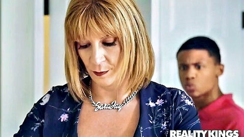 Mature blonde housewife in floral top stares down intently as young black stud glares from behind in interracial tension