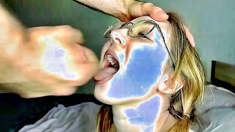 POV man's hand grips blonde woman's face in glasses forcing mouth wide open with tongue out