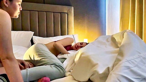 Asian women in intimate bedroom moment, one nude under sheets as lover leans close