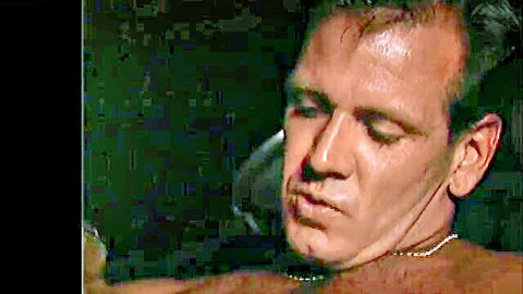 Shirtless man with collar, intense downward gaze in adult video thumbnail