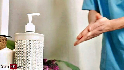 Closeup of hands lathering thick foamy soap suds from white dispenser in medical scrubs