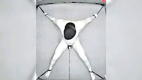 Naked man bound spread-eagle in BDSM bondage with CBT device clamping his exposed cock and balls