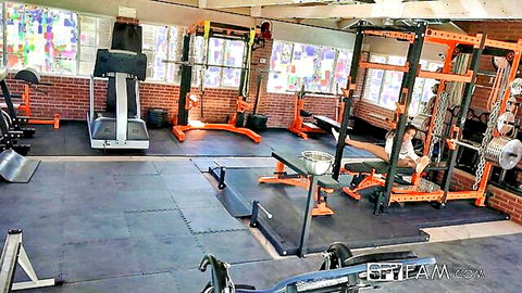 Empty gym interior with orange power racks treadmills and weights for hardcore workouts