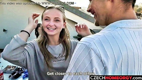 Smiling blonde babe in gray sweatshirt stands close to grinning guy outdoors on street teasing for Czech orgy