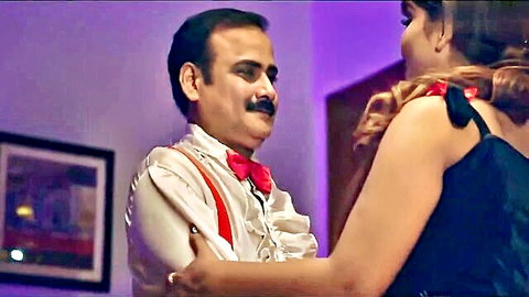 Older Indian man in suspenders and bowtie embraces busty South Asian woman's cleavage in intimate dance