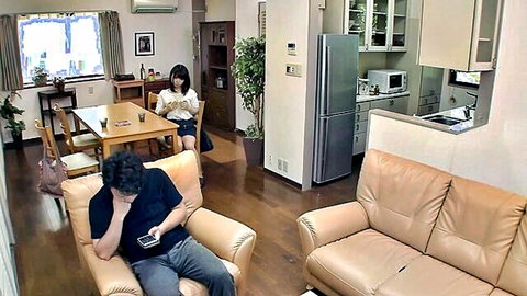 Japanese woman in short skirt sits at table reading while man on sofa checks phone covering face