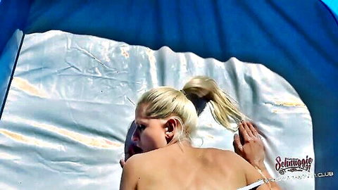 Topless blonde ponytail babe lies nude showing bare back and sideboob in white bikini bottoms inside beach tent
