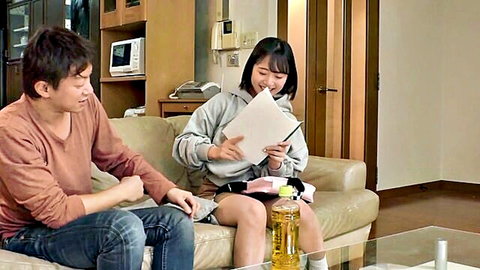 Cute Japanese babe in hoodie and skirt smiles holding papers next to boyfriend on couch amateur homemade