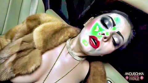 Brunette mistress Anoushka with green face paint lies back topless in fur coat exposing huge tits
