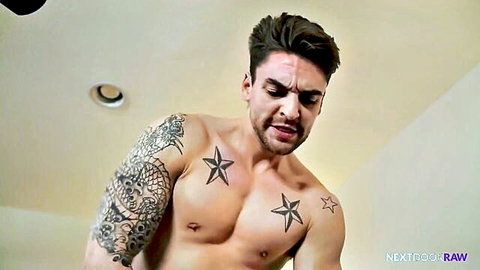 Muscular tattooed brunette hunk grimaces in pleasure showing ripped abs and star tattoos