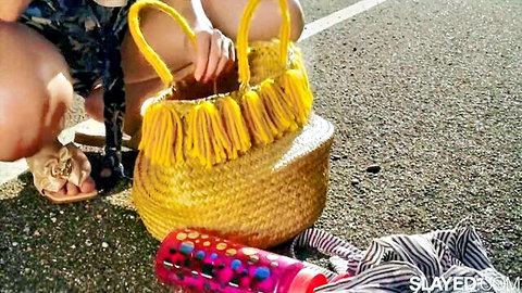Sexy young woman squats in short patterned dress holding yellow fringed bag on parking lot