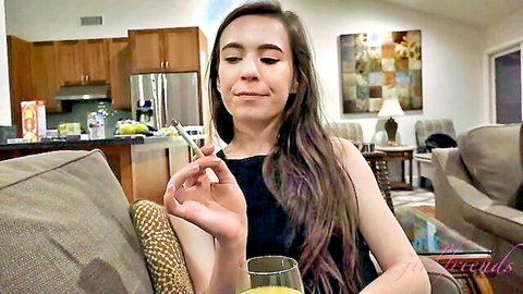 Seductive skinny brunette teen smokes cigarette teasingly on couch holding orange juice