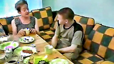 Chubby Russian mother-in-law in casual top at dinner table with younger man