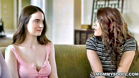 Two busty young brunettes showing deep cleavage chatting intimately on couch