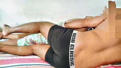 Two slim Tamil men lounging in swim trunks and black underwear on bed