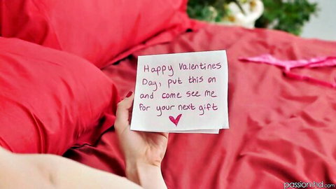 Woman's hand holds teasing Valentine's note 'put this on and come see me for pussy gift' on red bed