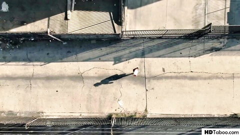 Aerial view of athletic woman in white shorts walking on cracked concrete rooftop with metal fences